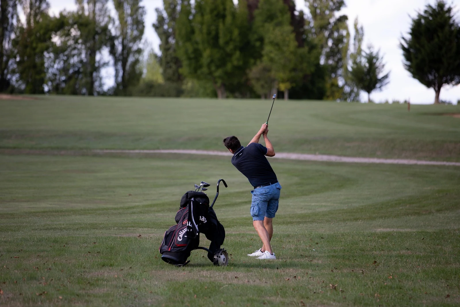 A golfer playing a shot beside a golf bag